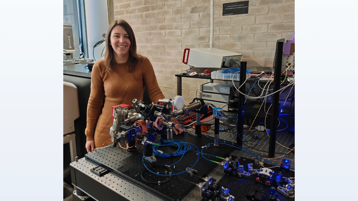 Image of Dr Mega Garner-Smith next to a cold atom clock that she is developing